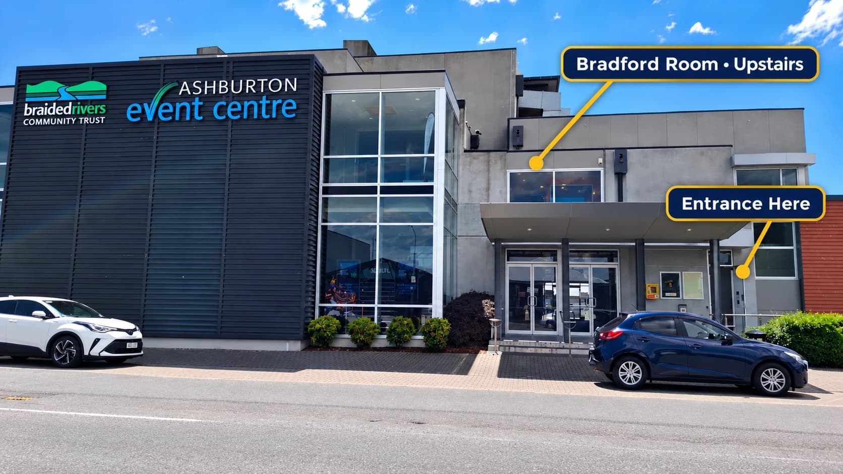 The Ashburton Event Centre from Wills Street on a clear day. One label points to the upstairs Bradford Room windows; another, labelled Entrance Here, points to the smaller door to the right of the main glass doors.